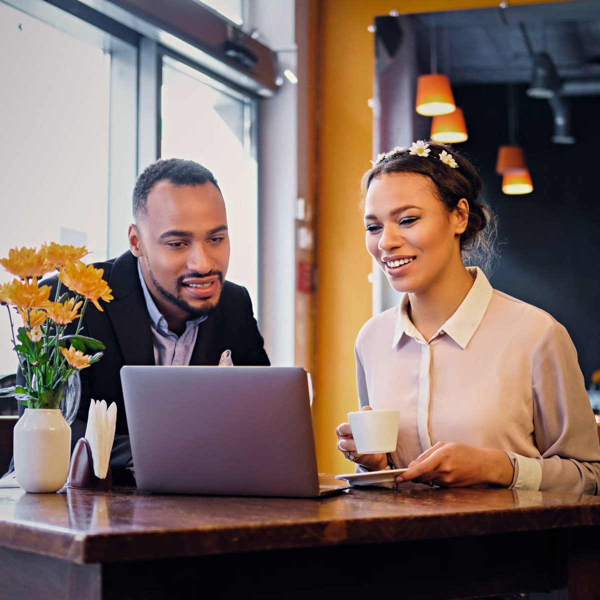 Black African American business male and female drinks coffee and using a laptop in a restaurant.