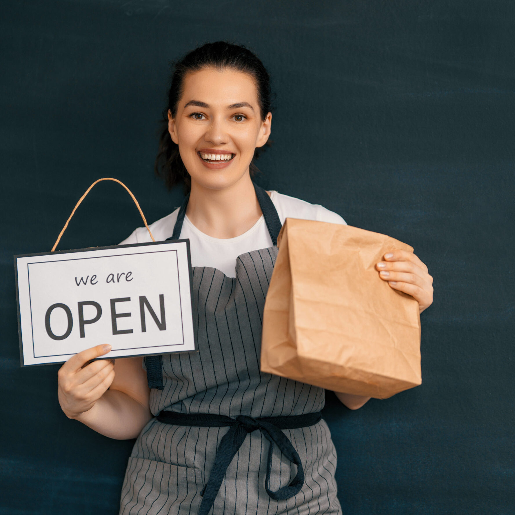 Business woman holding "We are open" sign with curbside pick-up bag.