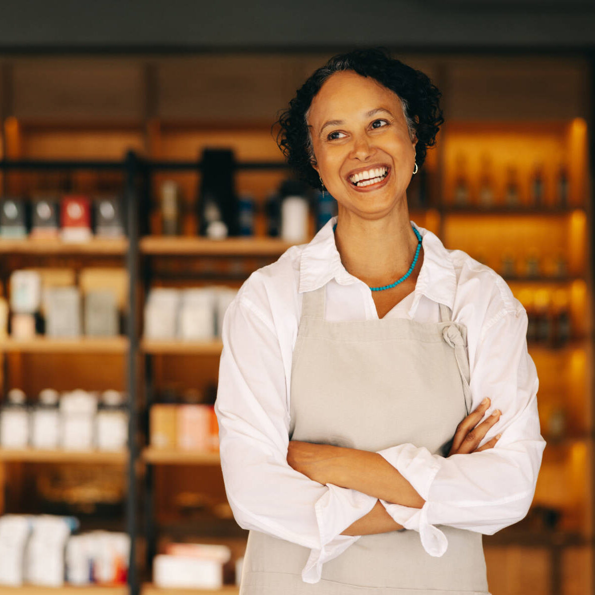 Successful small business owner smiling happily while standing at the entrance of her grocery store with her arms crossed. Mature entrepreneur running a trendy convenience store.