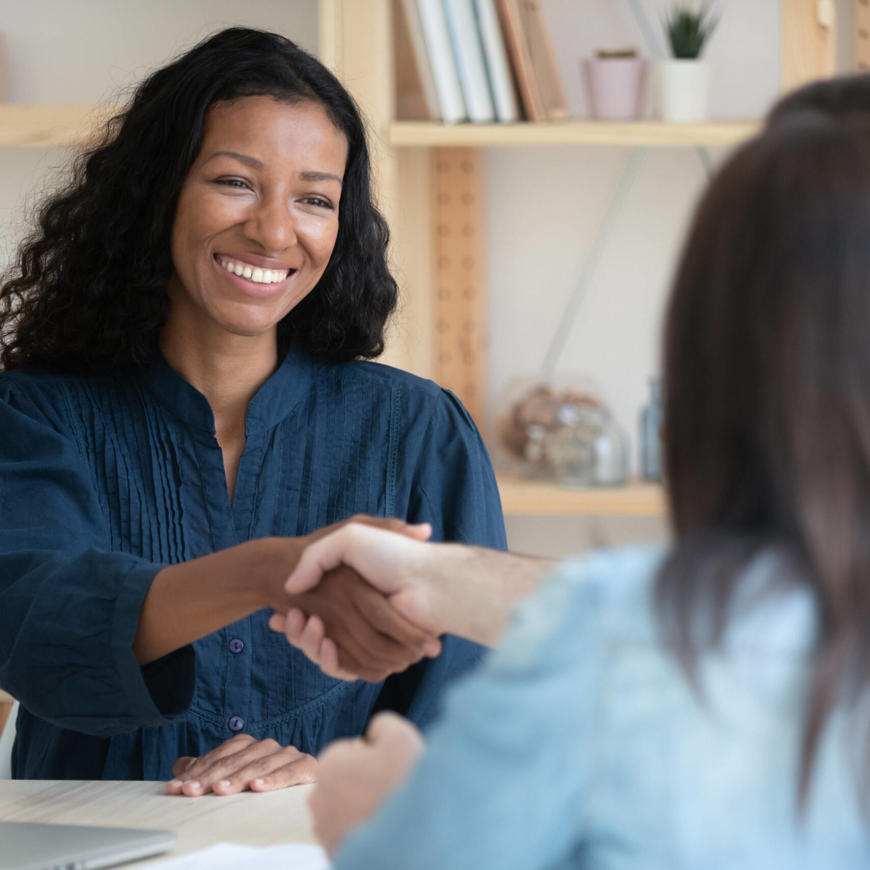 Smiling African American woman shake hand of couple clients at business meeting in office. Back view of recruiters handshake biracial female candidate get acquainted or close deal at negotiation.