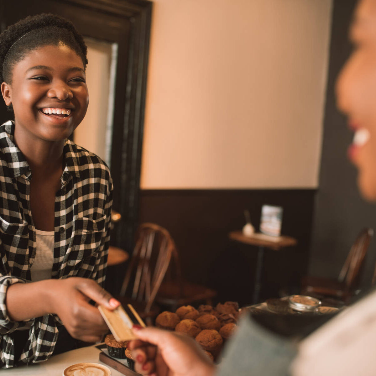 Smiling young African woman giving her bank card to a cafe cashier pay for her cappuccino