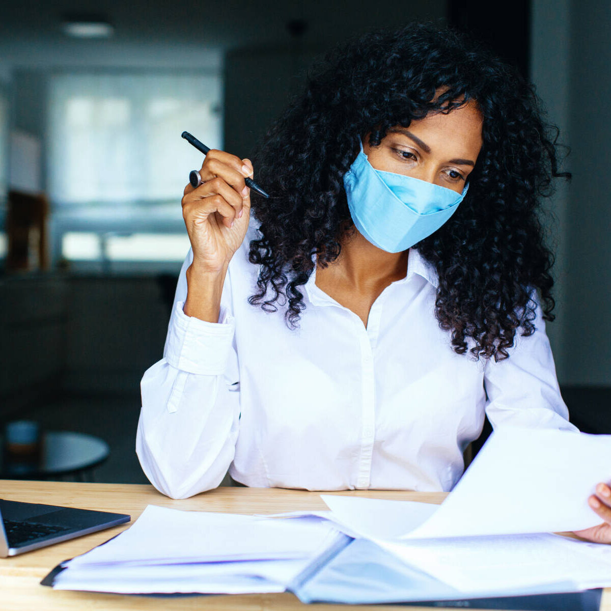 Portrait of a person working sitting at desk wearing mask, reading paper bill or contract